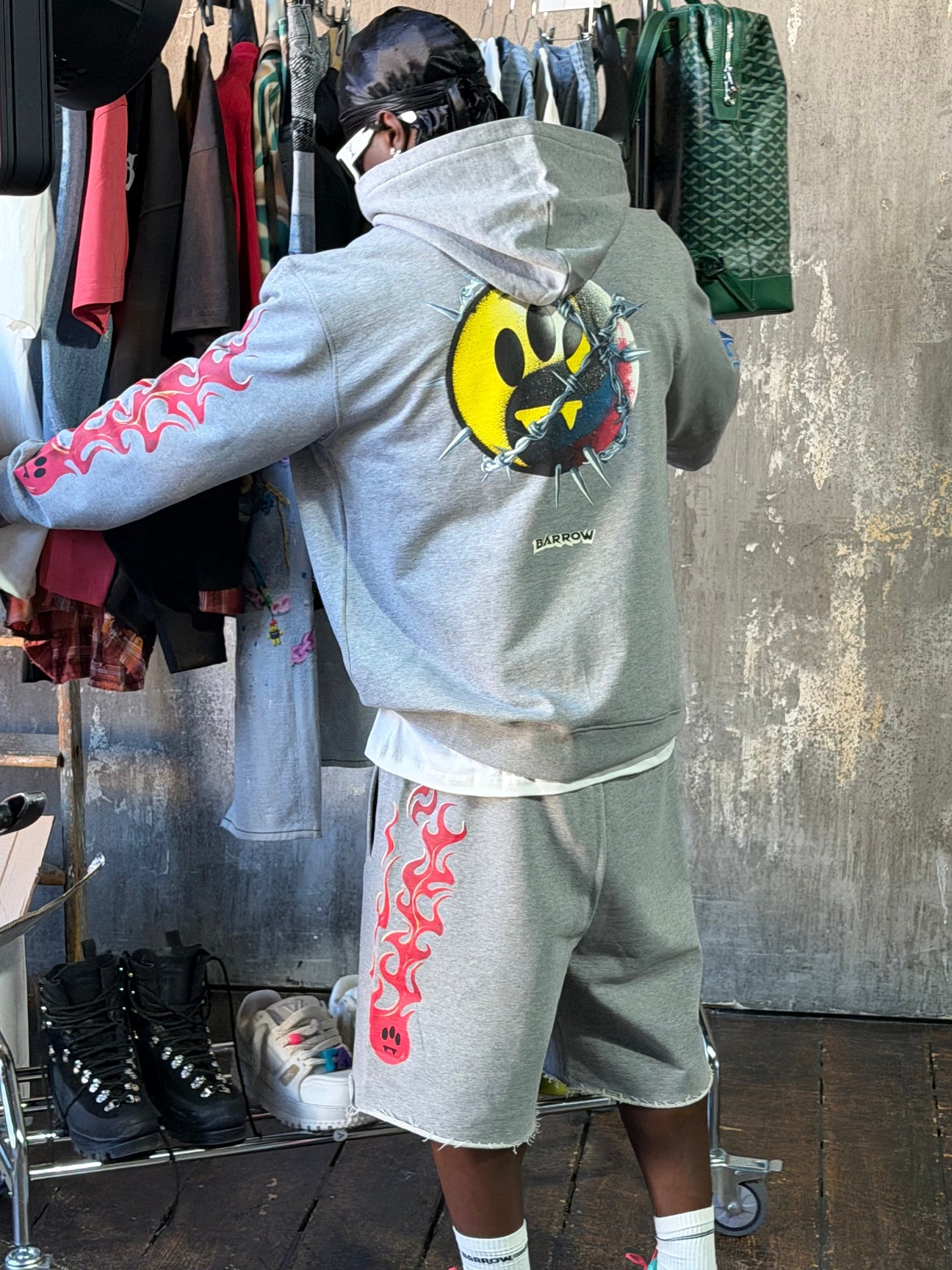 Conjunto Barrow streetwear de lujo: hoodie gris con smiley de tres ojos y llamas rosas, look completo en tienda urbana.