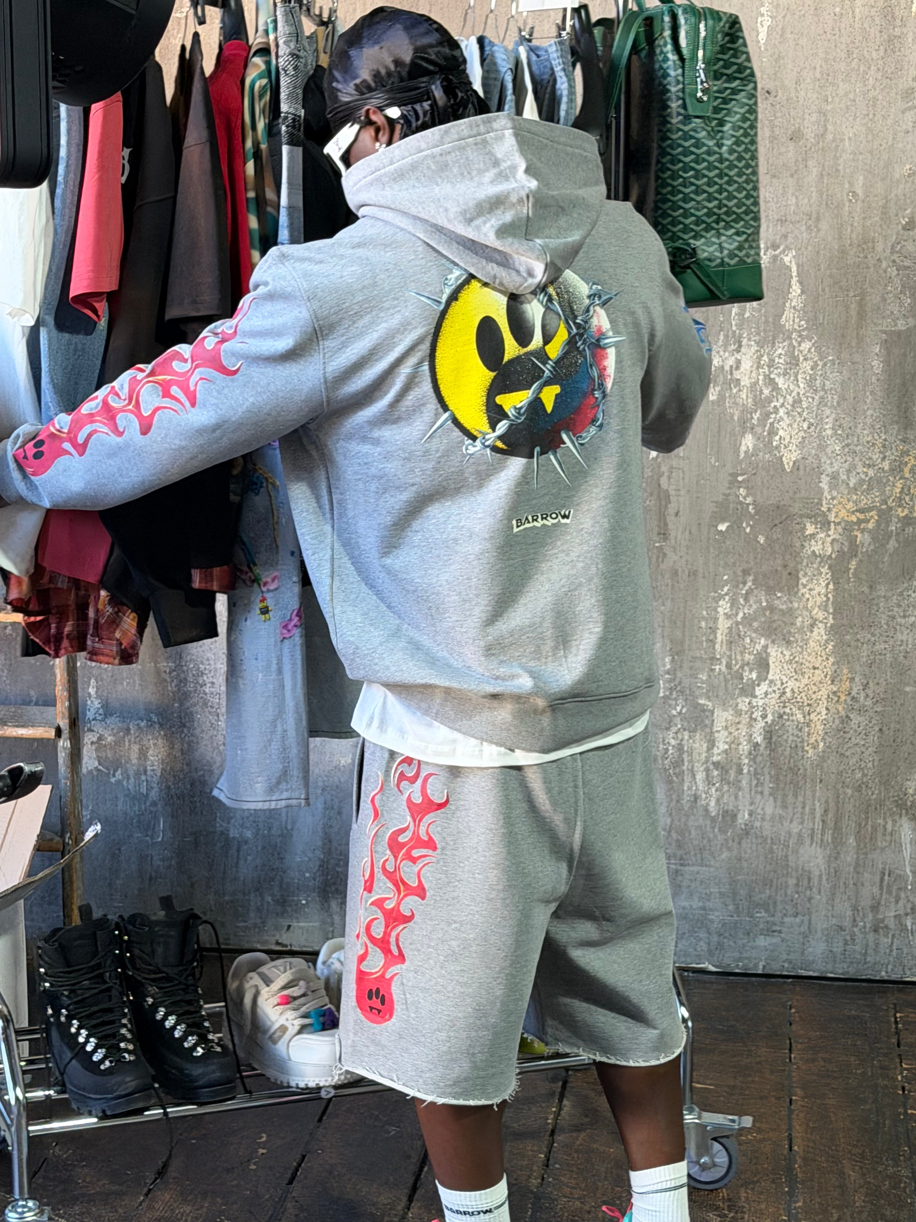 Conjunto Barrow streetwear de lujo: hoodie gris con smiley de tres ojos y llamas rosas, look completo en tienda urbana.