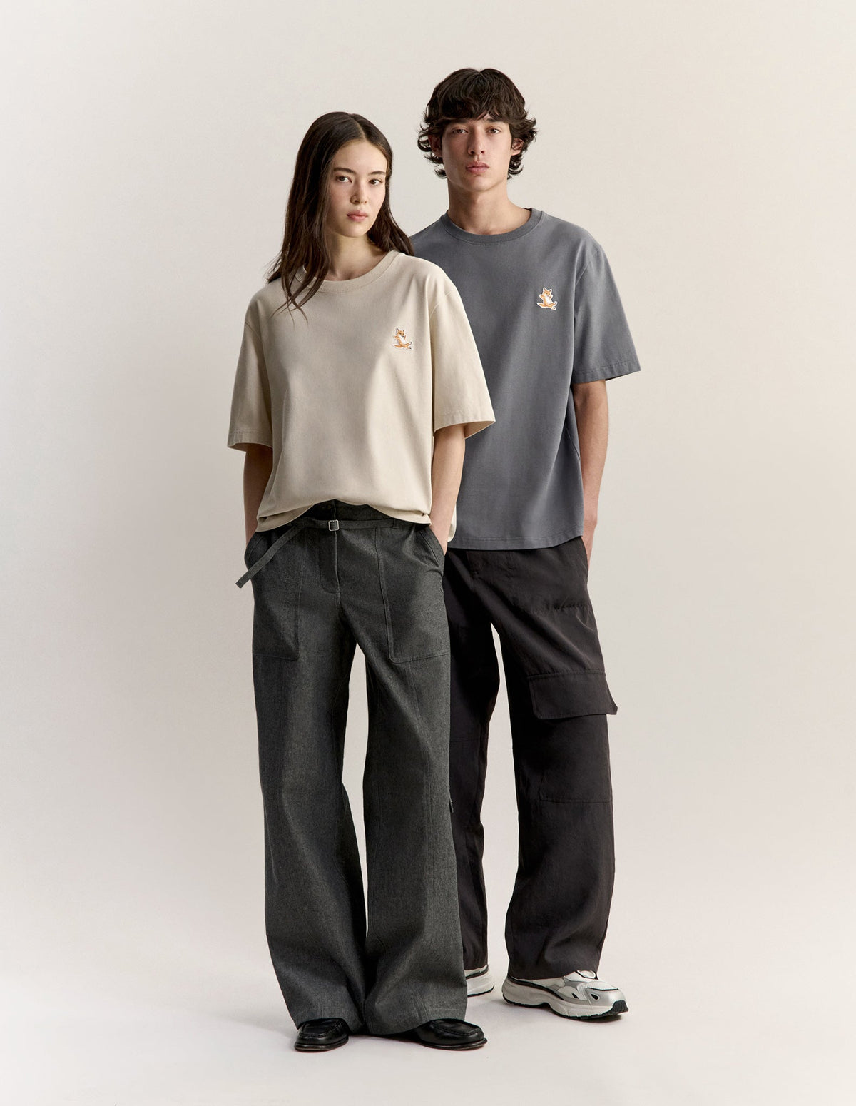 Dos modelos con camisetas Maison Kitsuné en beige y gris con el zorro bordado en el pecho.