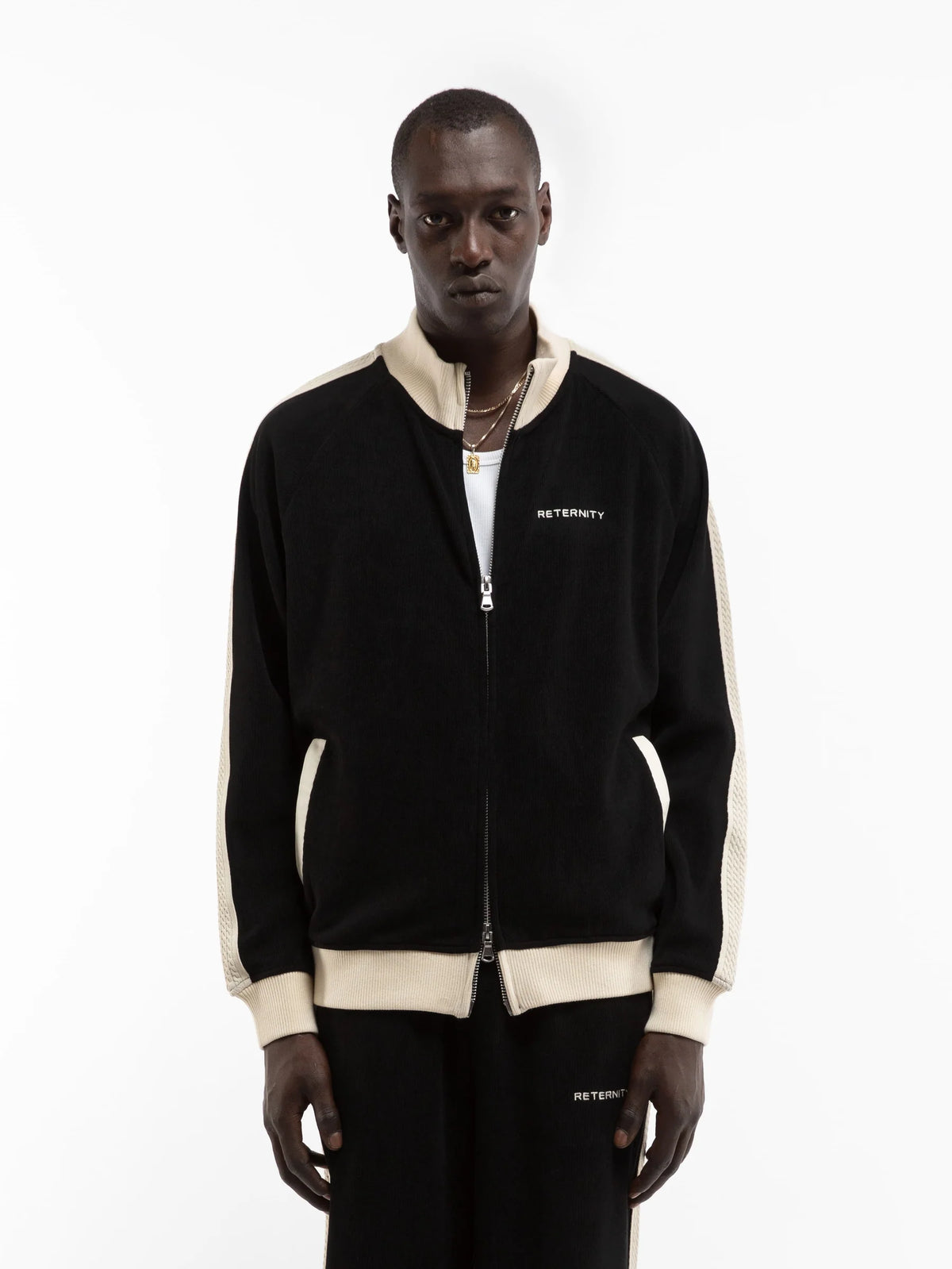 Hombre con la chaqueta Reternity Studio Knit Track negra con ribetes crema y pantalón a juego, look completo