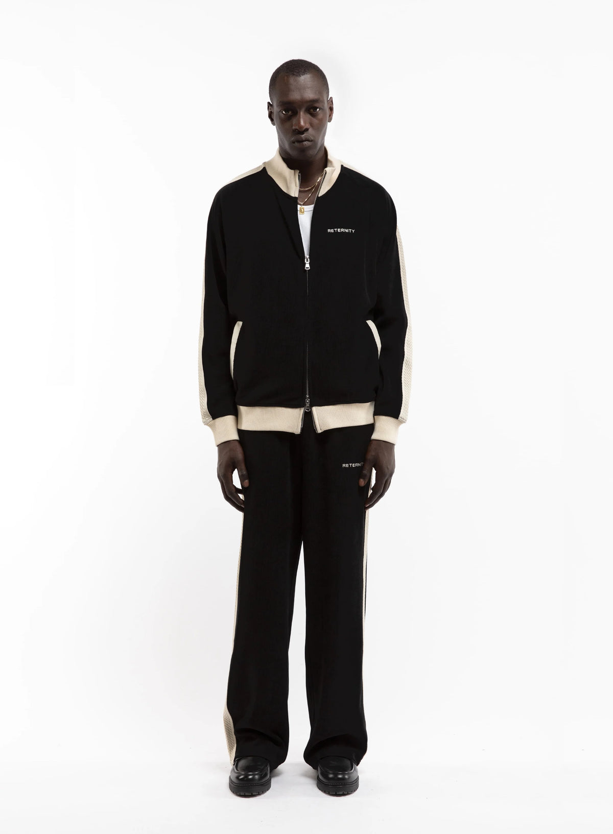 Hombre con la chaqueta Reternity Studio Knit Track negra con ribetes crema, cuerpo entero