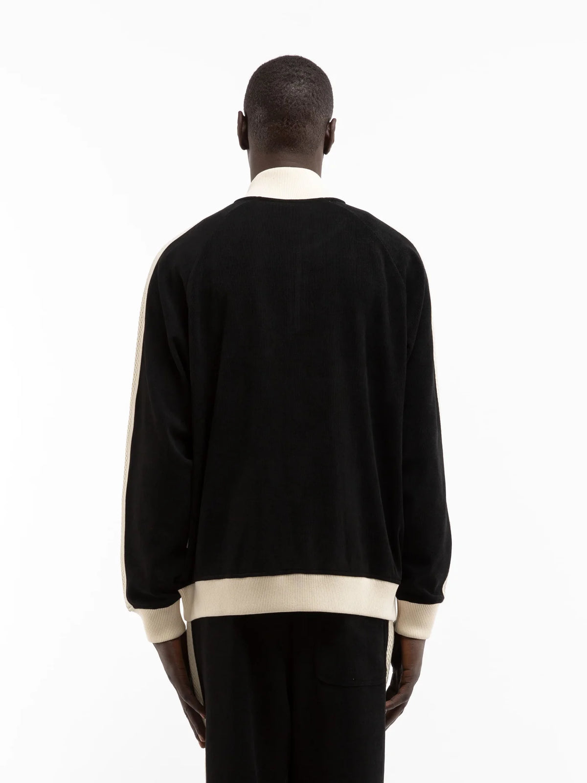 Hombre de espaldas con la chaqueta Reternity Studio Knit Track negra con ribetes crema y bajo en contraste, cuerpo entero