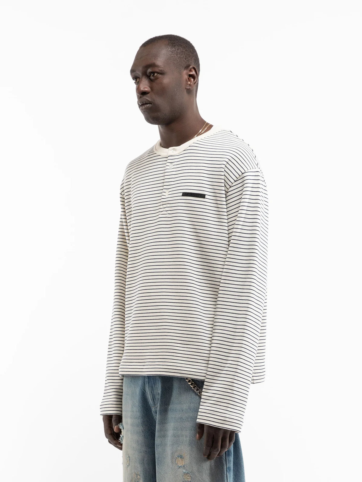 Modelo con camiseta Reternity Henley Stripe en crudo y azul marino, detalle de la etiqueta en el pecho