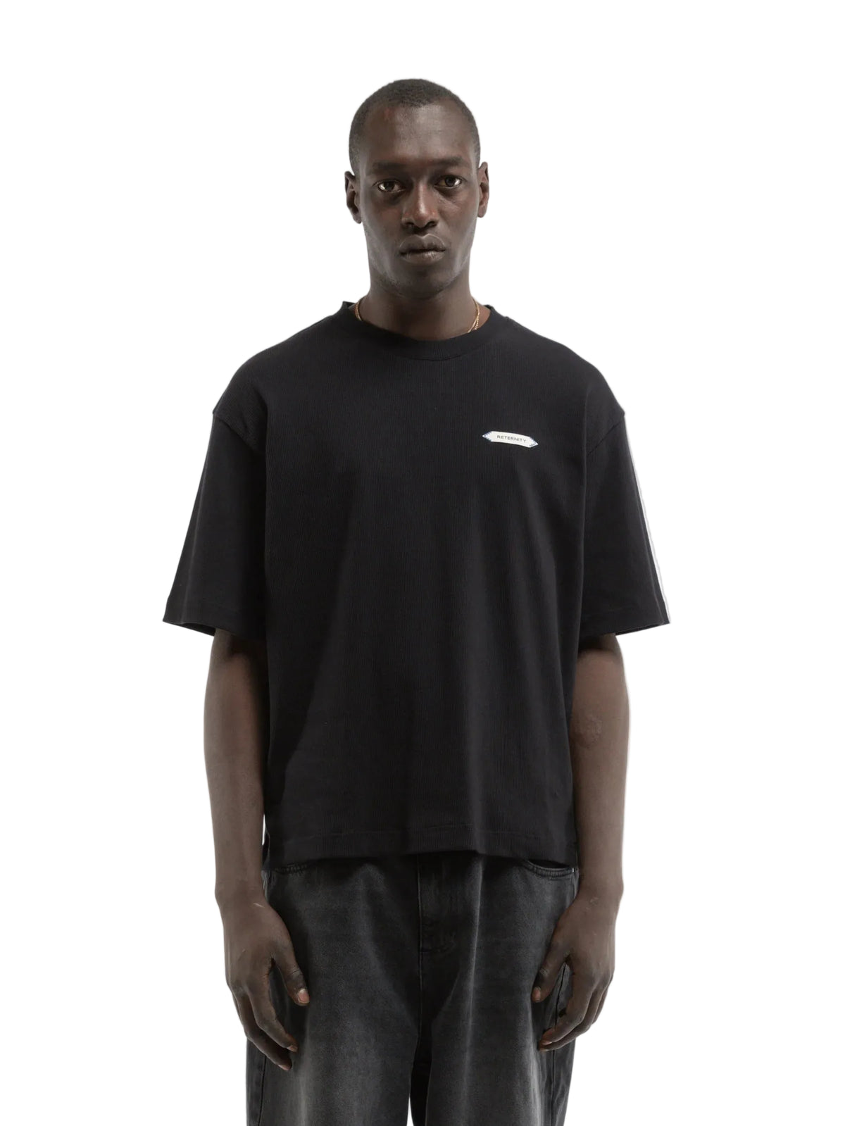 Hombre con la camiseta Reternity L'Atelier Line Rib negra y pantalón claro, look completo de cuerpo entero