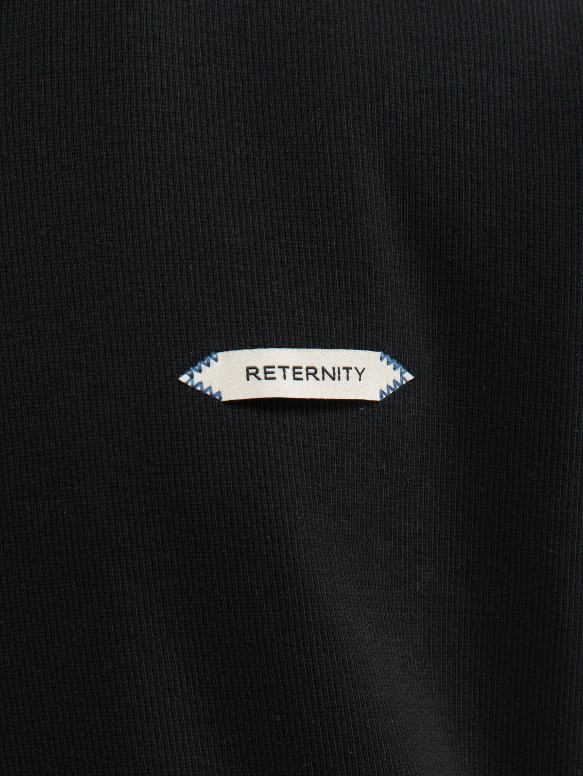 Detalle de la etiqueta oval RETERNITY sobre el pecho de la sudadera negra