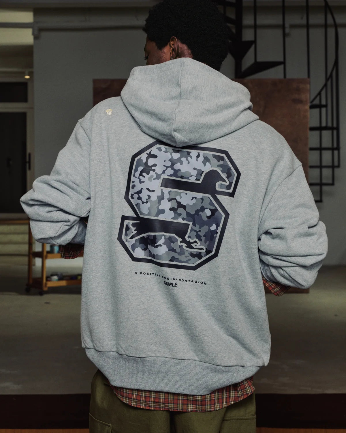 Hombre de espaldas con la sudadera Staple Pigeon Sport gris mostrando el gráfico trasero