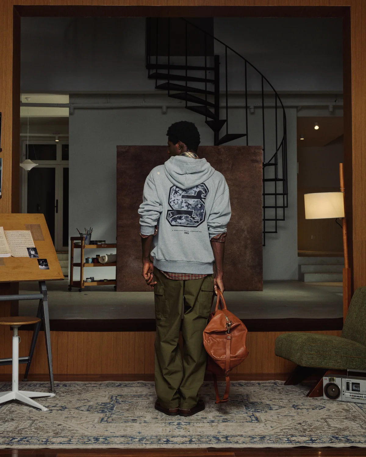 Hombre con la sudadera Staple Pigeon Sport gris jaspeado, vista de espalda con el gráfico de la S