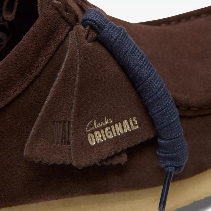 Detalle de la etiqueta Clarks Originals en la lengüeta de la Wallabee en ante marrón oscuro con cordones azul marino