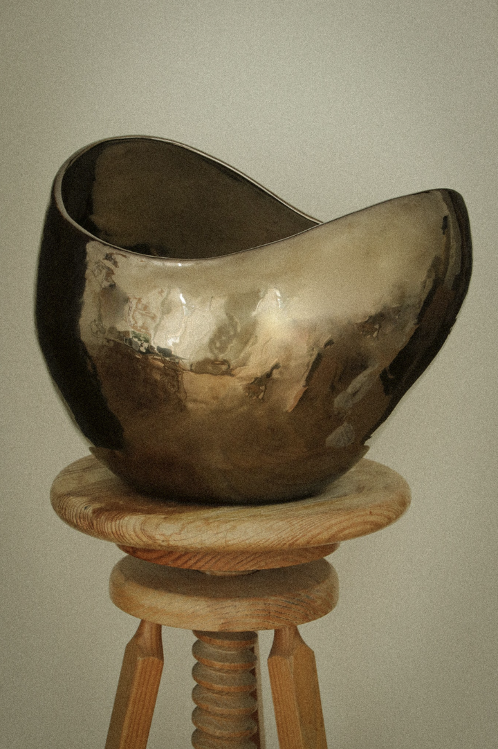 Vela escultura AMBER LIGHT de AMEN en dorado metálico, sobre un taburete de madera