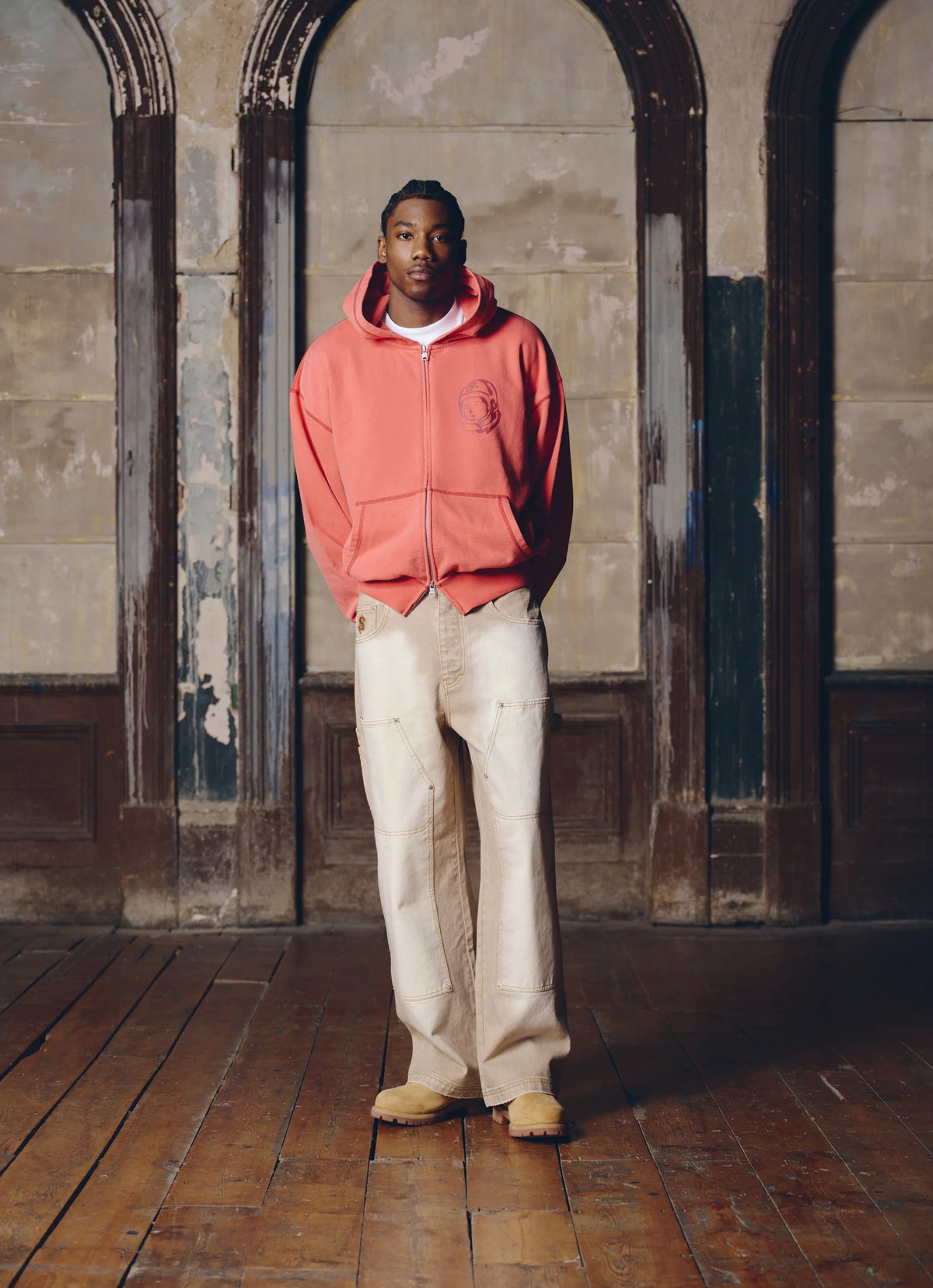 Hombre con la sudadera con capucha y cremallera Billionaire Boys Club roja y pantalón claro, look completo de cuerpo entero