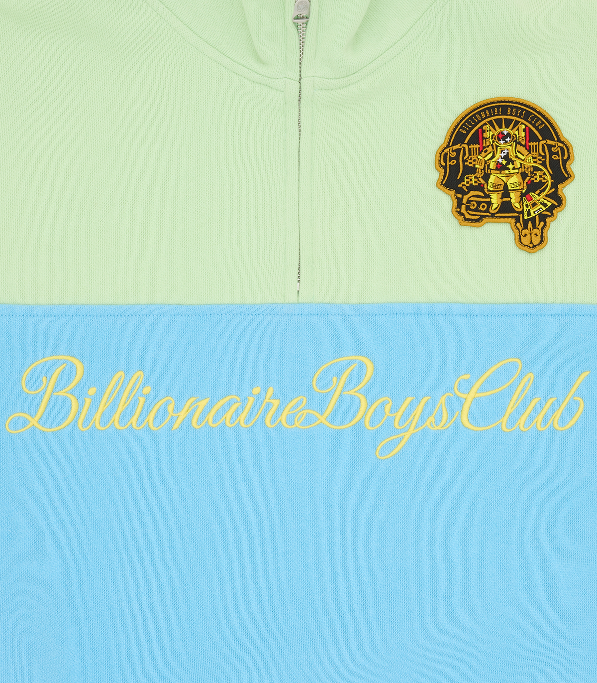 Detalle del script Billionaire Boys Club en dorado y el parche del astronauta sobre el panel azul de la sudadera verde menta