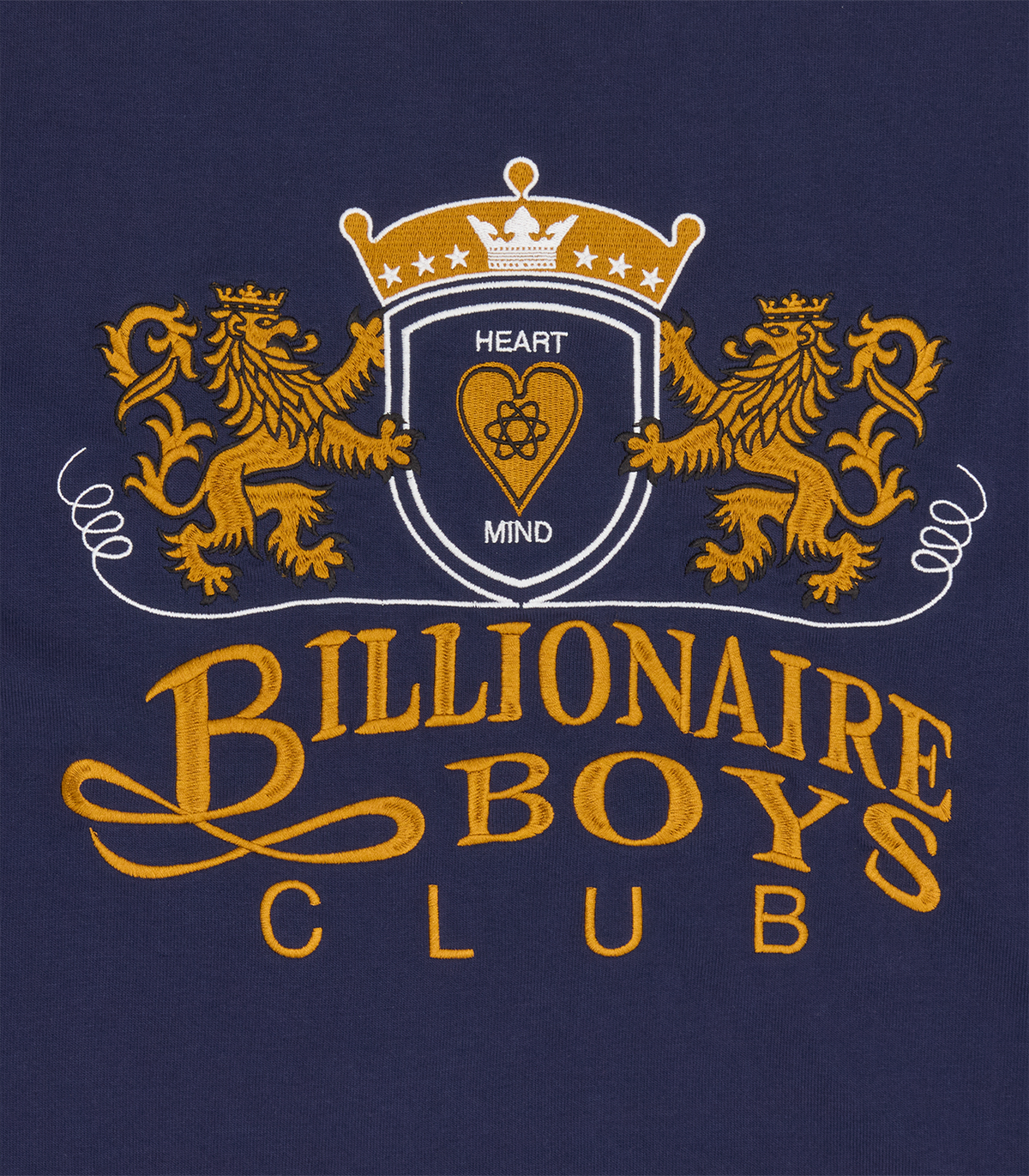 Detalle del escudo con dos leones bordado, corona y BILLIONAIRE BOYS CLUB en dorado sobre la camiseta azul marino