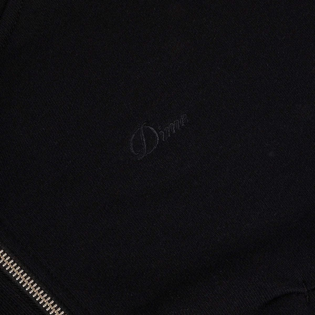 Detalle del logo Dime bordado al tono y la cremallera metálica de la sudadera negra