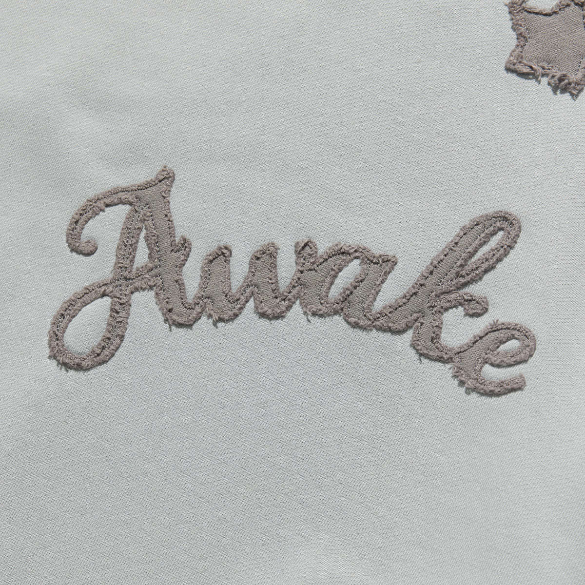 Detalle del lettering Awake en cursiva bordado sobre la sudadera gris jaspeado