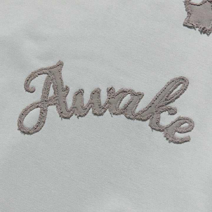 Detalle del lettering Awake en cursiva bordado sobre la sudadera gris jaspeado