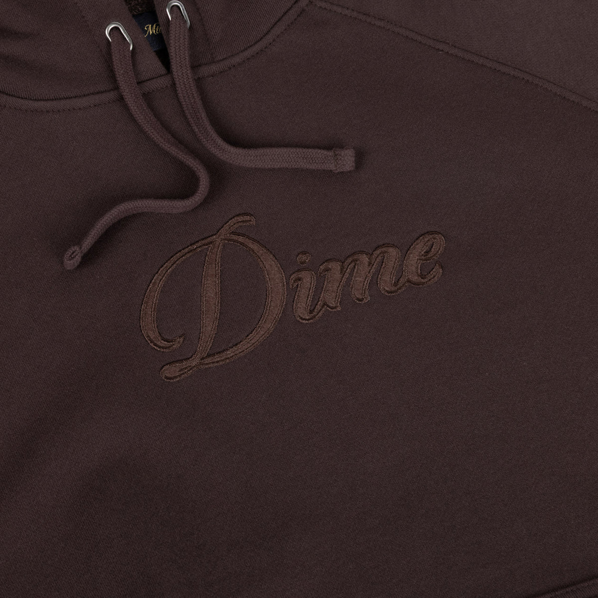 Detalle del logo Dime en cursiva bordado al tono sobre el parche de fieltro de la sudadera marrón