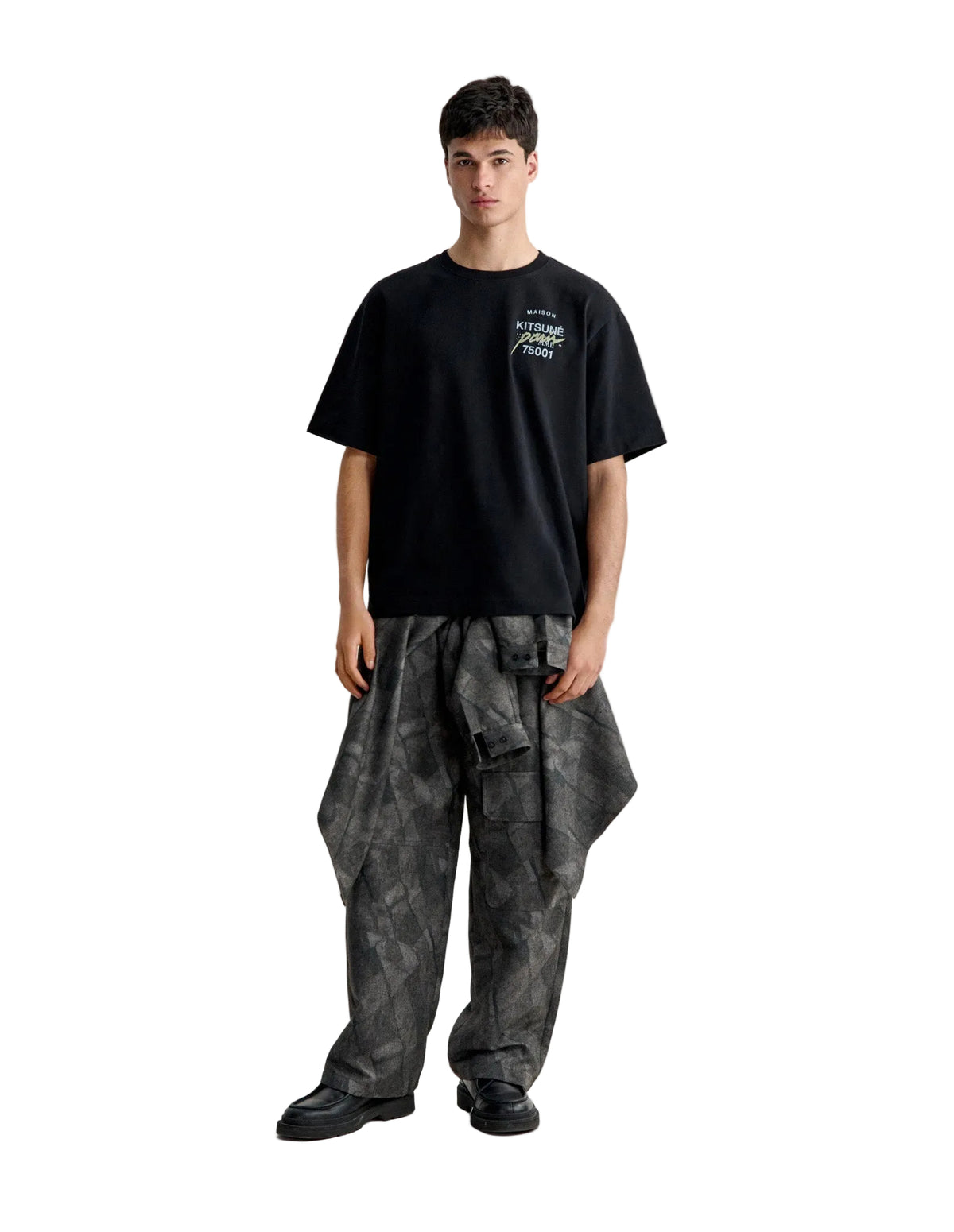 Hombre con la camiseta Maison Kitsuné MMII oversize negra y pantalón estampado, vista de cuerpo entero