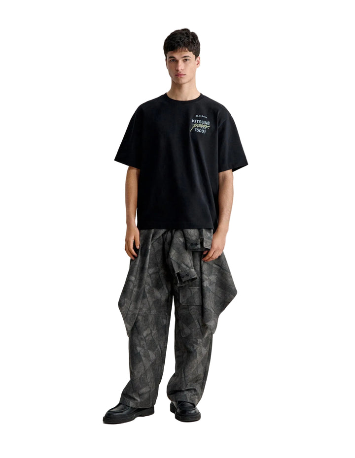 Hombre con la camiseta Maison Kitsuné MMII oversize negra y pantalón estampado, vista de cuerpo entero