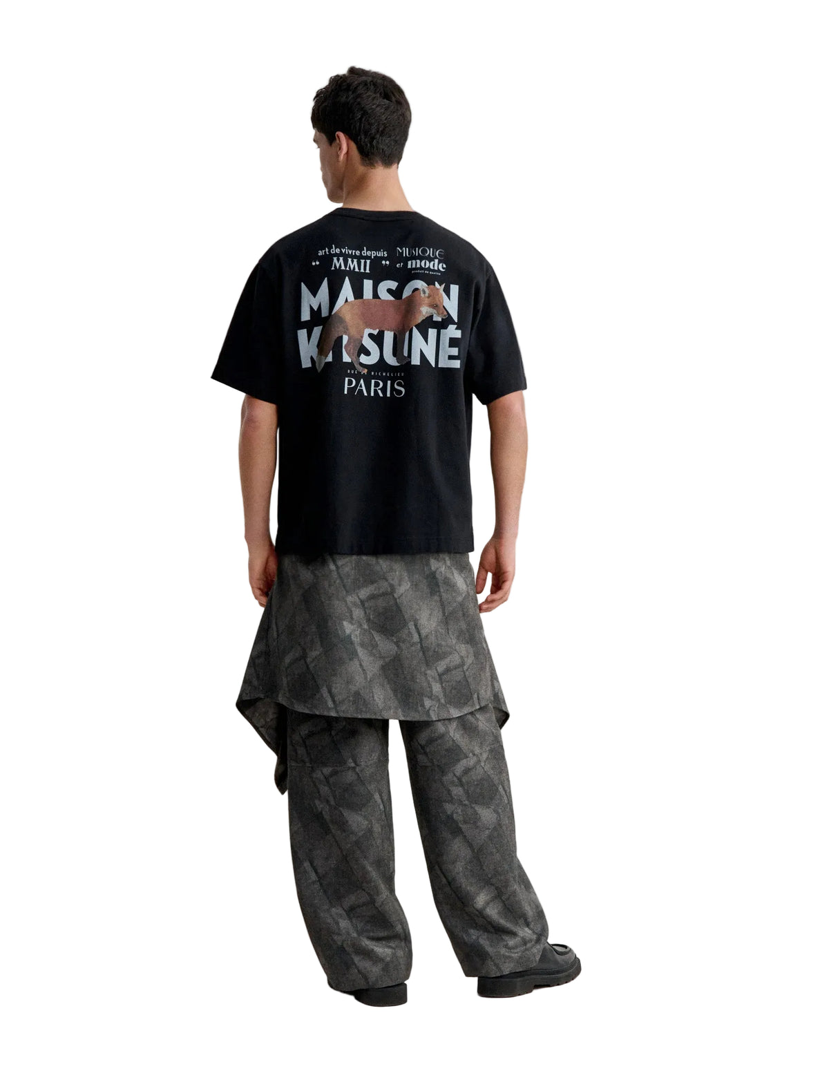 Hombre de espaldas con la camiseta Maison Kitsuné MMII oversize negra y el logo MAISON KITSUNÉ PARIS en la espalda, cuerpo entero