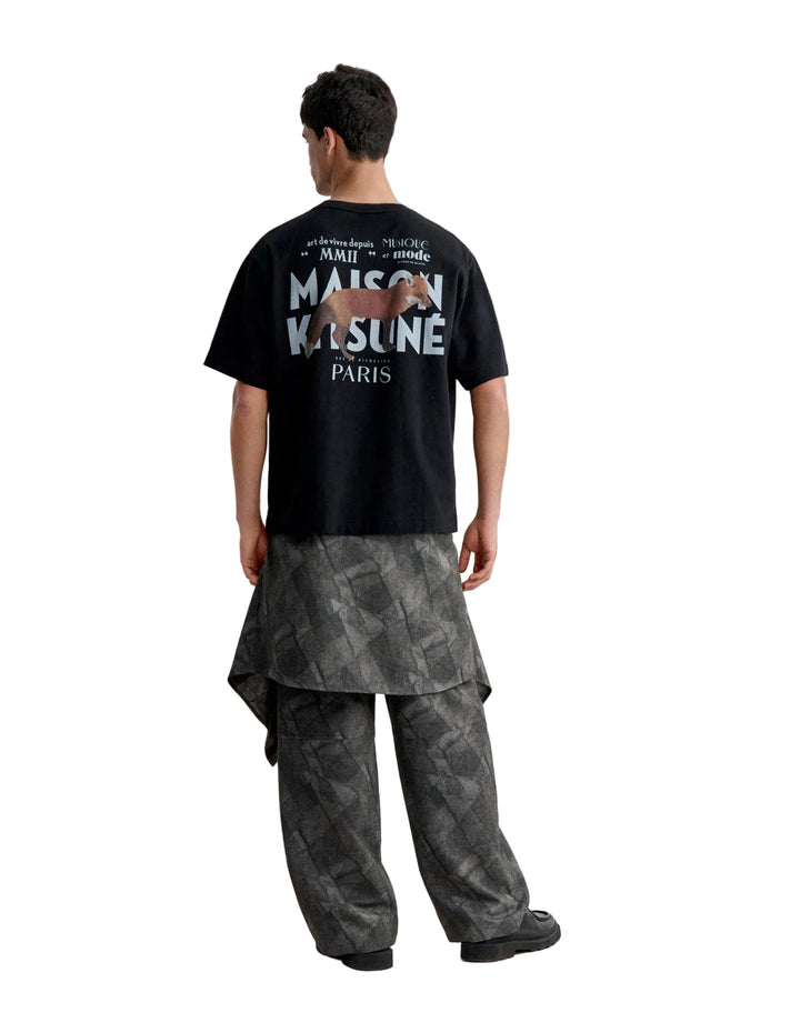 Hombre de espaldas con la camiseta Maison Kitsuné MMII oversize negra y el logo MAISON KITSUNÉ PARIS en la espalda, cuerpo entero