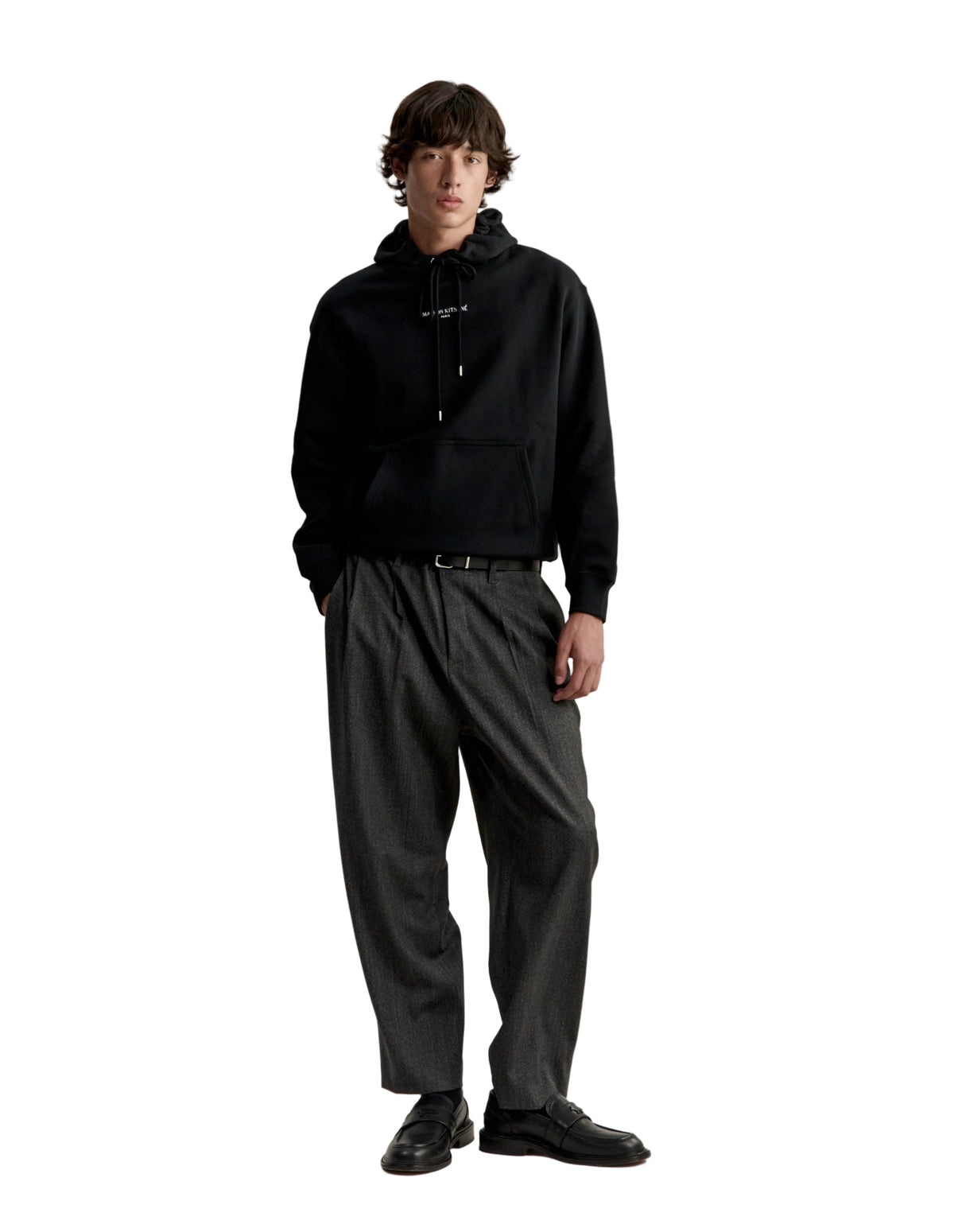 Hombre con la sudadera con capucha Maison Kitsuné Paris Comfort negra y pantalón gris, vista de cuerpo entero