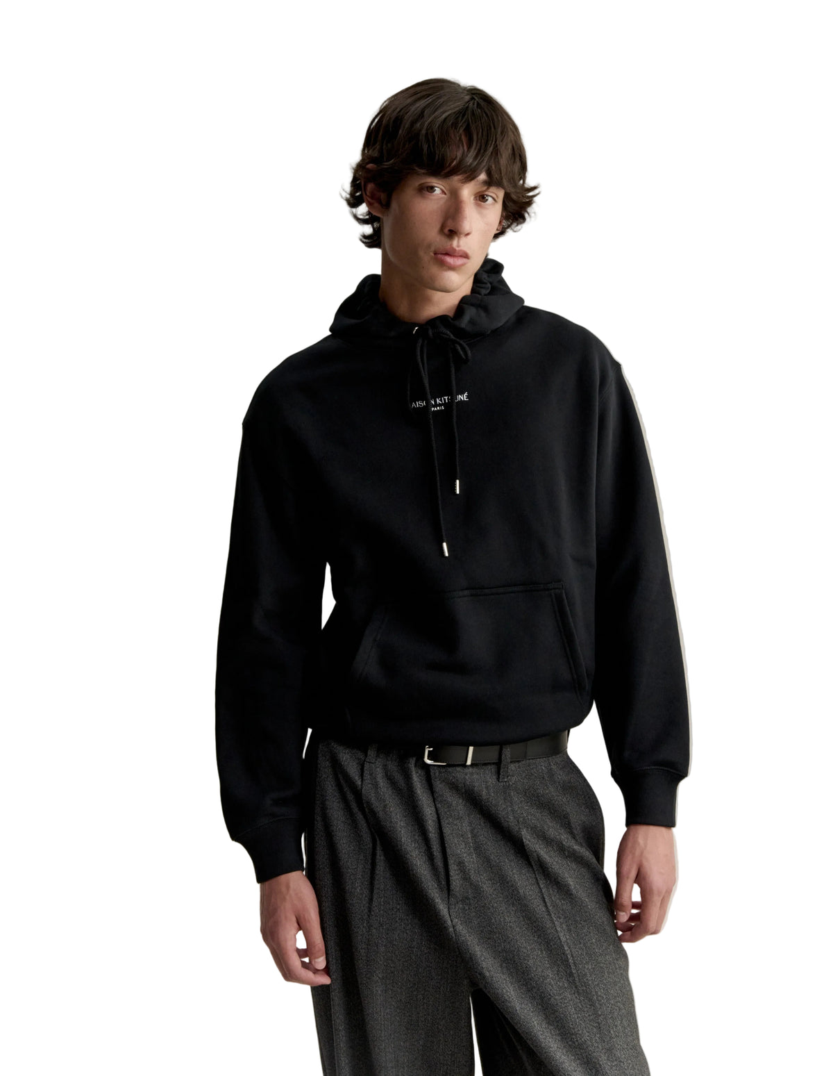 Hombre con la sudadera con capucha Maison Kitsuné Paris Comfort negra y pantalón gris, look completo