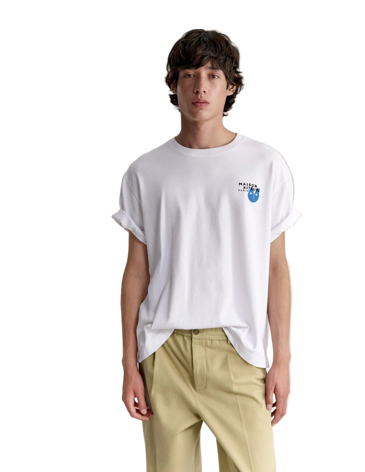 Hombre con la camiseta Maison Kitsuné Fortune Fox blanca y pantalón claro, look completo de cuerpo entero