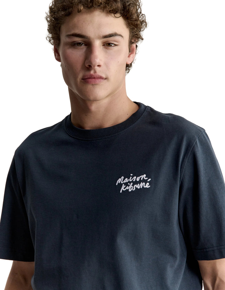 Hombre con la camiseta Maison Kitsuné Handwriting azul marino, plano de medio cuerpo con el logo manuscrito en el pecho