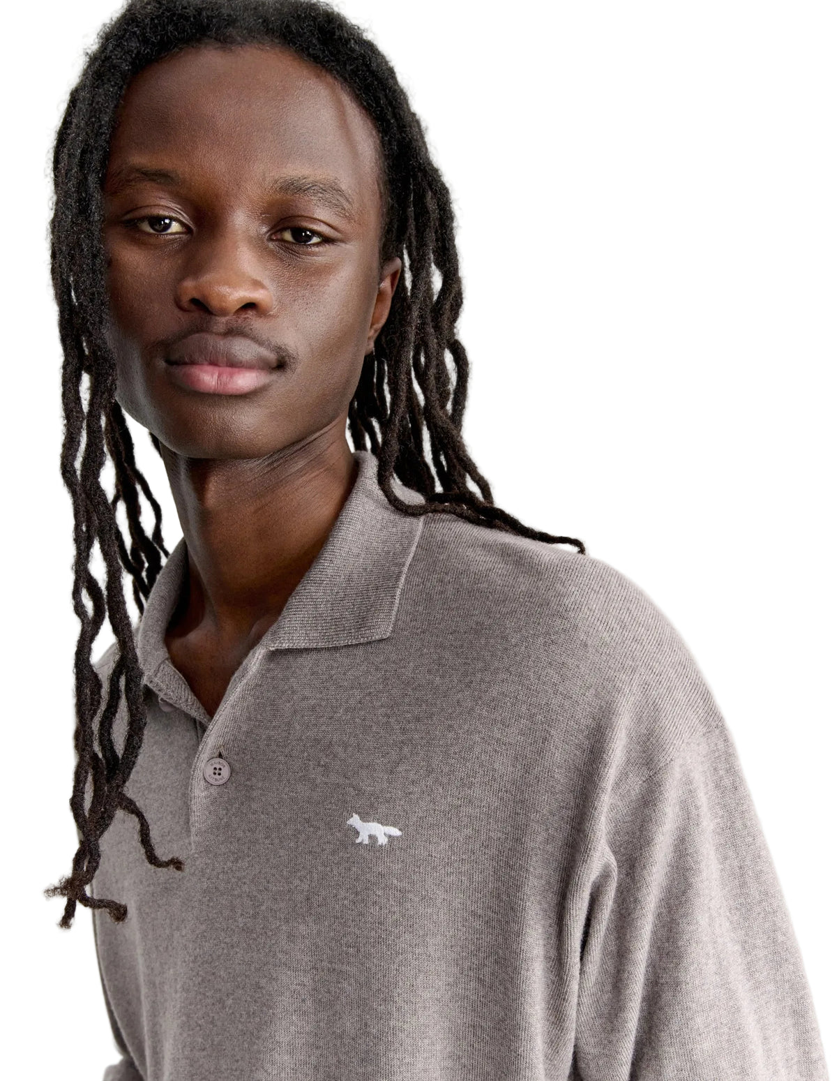 Hombre con el polo de punto Maison Kitsuné beige, plano de medio cuerpo con el zorro de perfil bordado en el pecho