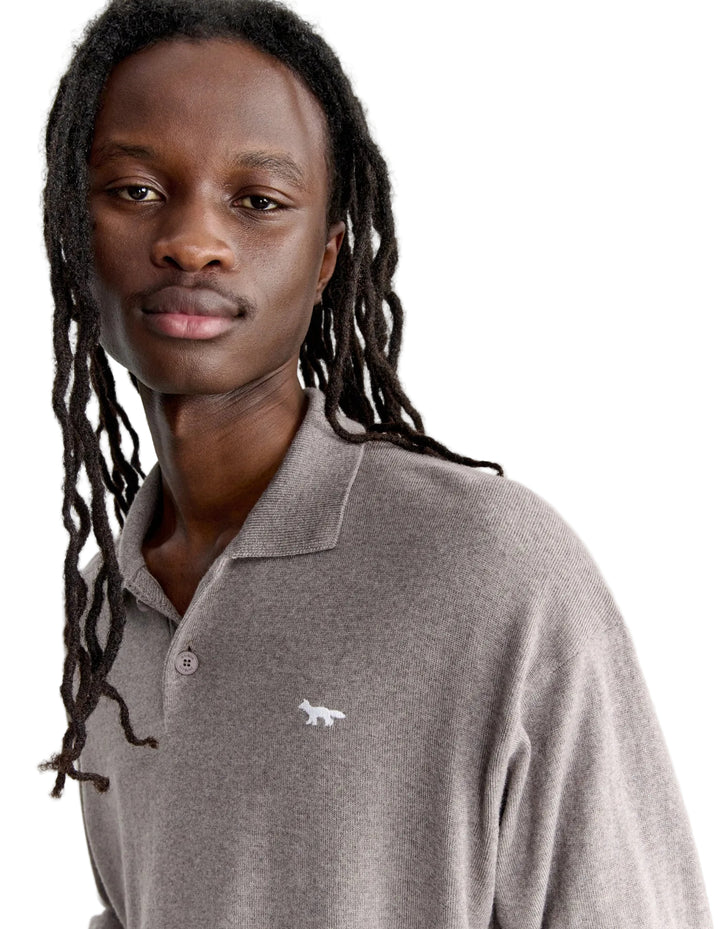 Hombre con el polo de punto Maison Kitsuné beige, plano de medio cuerpo con el zorro de perfil bordado en el pecho