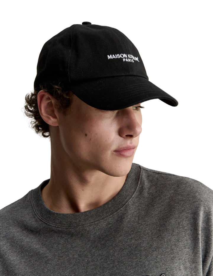 Hombre con la gorra Maison Kitsuné Paris negra, plano de medio cuerpo de perfil