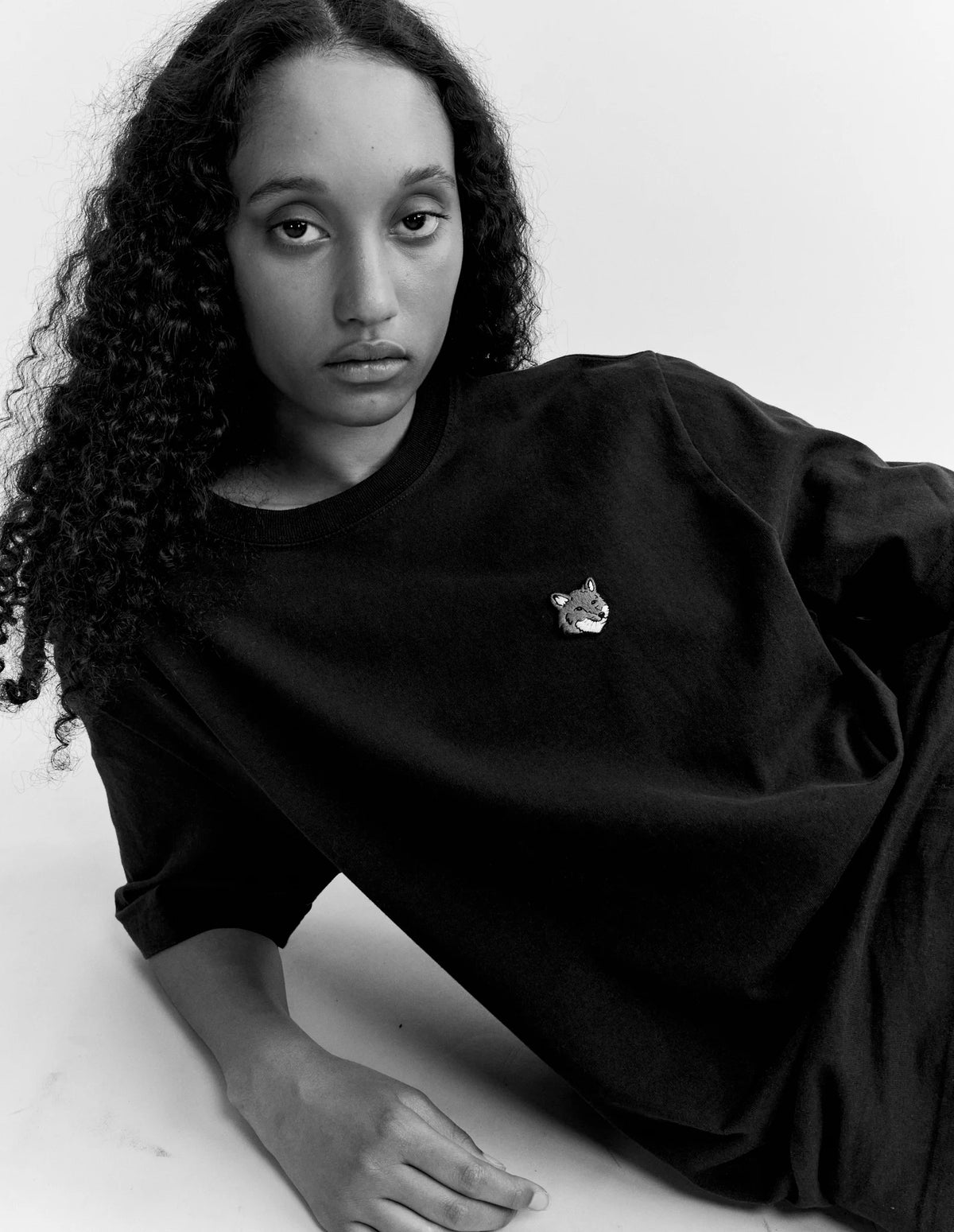 Persona tumbada con la camiseta Maison Kitsuné Fox Head, fotografía en blanco y negro