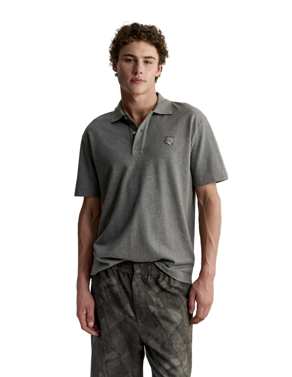 Hombre con el polo Maison Kitsuné Fox Head Comfort gris y pantalón oscuro, look completo