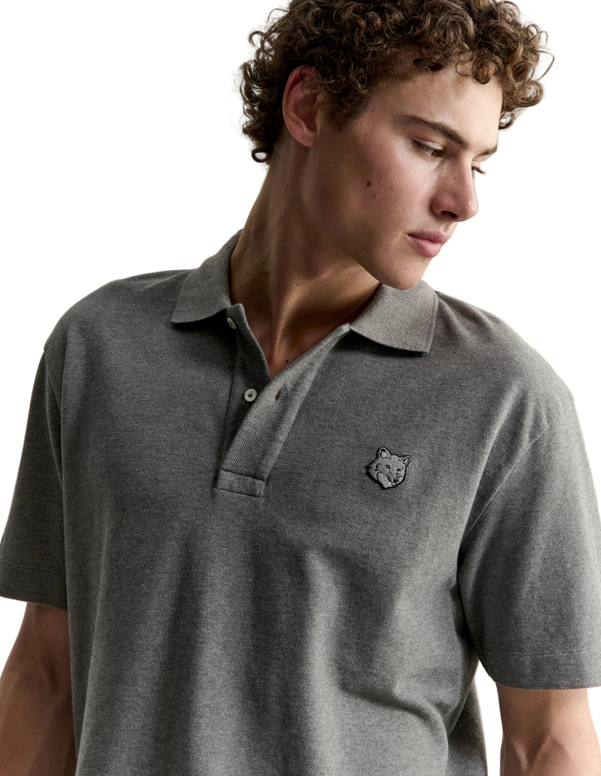 Hombre con el polo Maison Kitsuné Fox Head Comfort gris, plano de medio cuerpo con el parche del zorro en el pecho