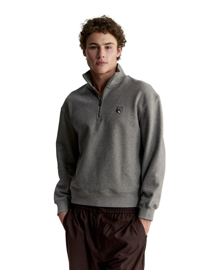 Hombre con la sudadera Maison Kitsuné Fox Head Half-Zip gris y pantalón oscuro, look completo