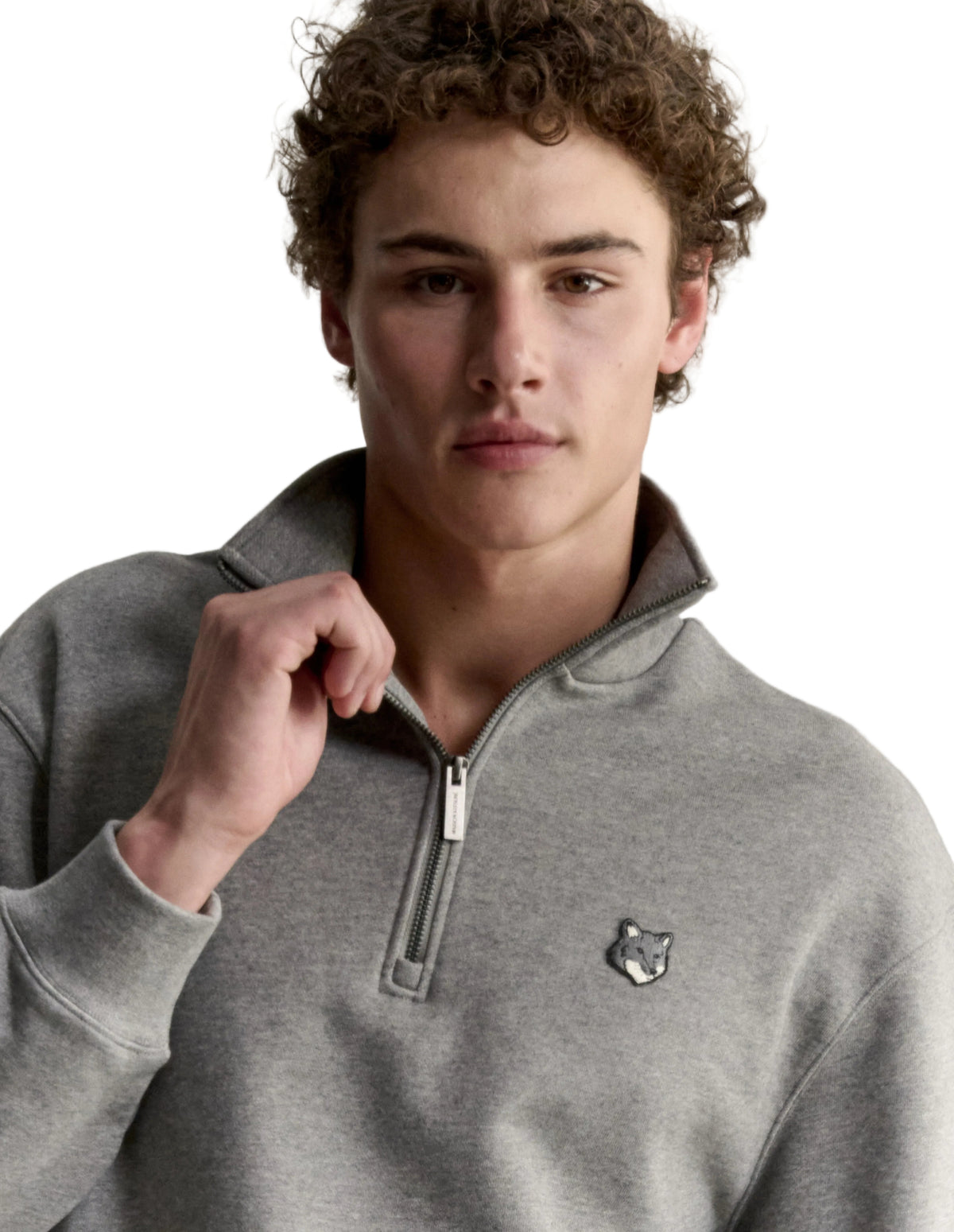 Hombre con la sudadera Maison Kitsuné Fox Head Half-Zip gris, plano de medio cuerpo con el parche del zorro en el pecho
