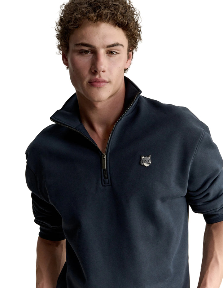 Hombre con la sudadera Maison Kitsuné Fox Head Half-Zip azul marino, plano de medio cuerpo con el parche del zorro en el pecho