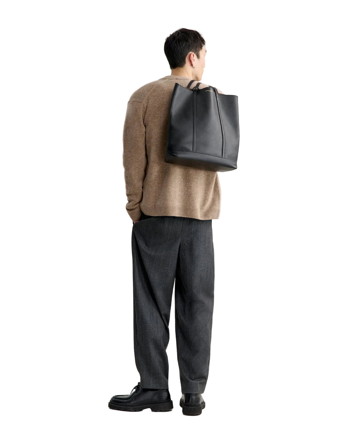 Hombre de espaldas con el cárdigan Maison Kitsuné Fox Head Lambswool beige, pantalón oscuro y bolsa al hombro, cuerpo entero
