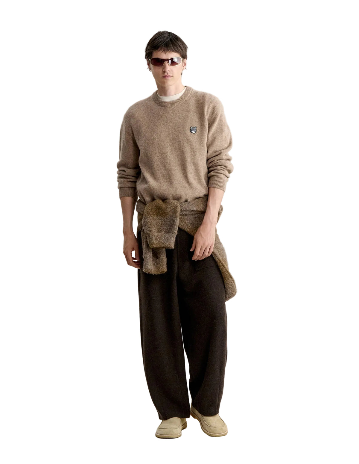 Hombre con el jersey Maison Kitsuné Fox Head Lambswool beige, prenda atada a la cintura y pantalón marrón, cuerpo entero