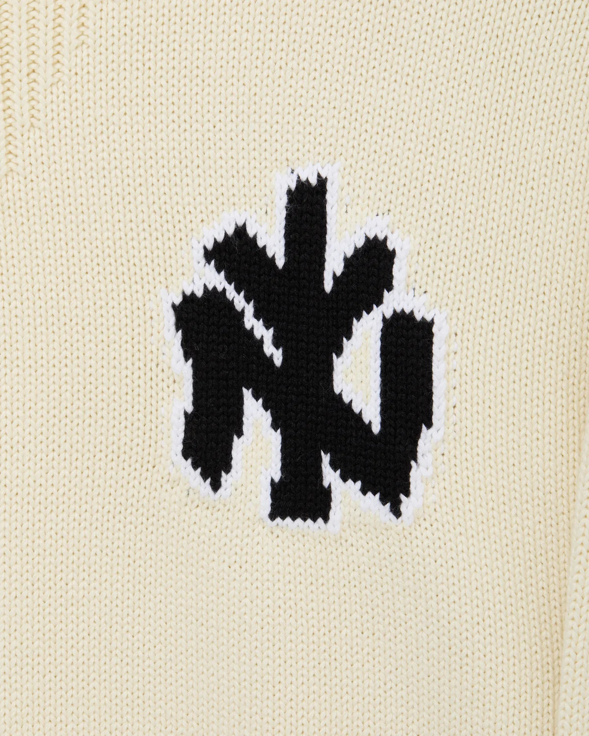Detalle del logo NY tejido en intarsia negro sobre el jersey de punto Staple crema