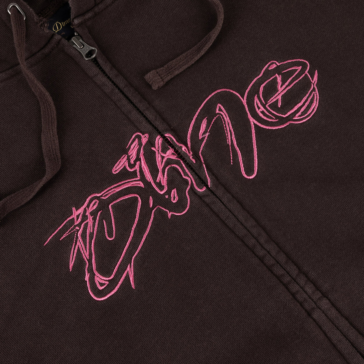 Detalle del logo Dime bordado en estilo grafiti rosa sobre la sudadera marrón lavada