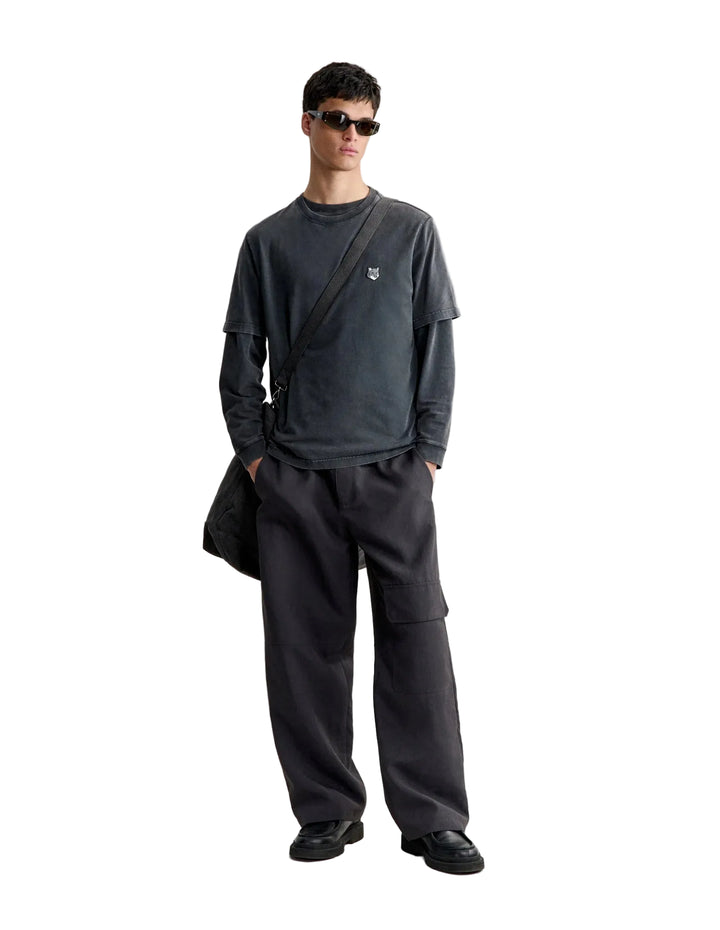 Hombre con la camiseta Maison Kitsuné Fox Head Faded en gris oscuro y pantalón gris, look completo de cuerpo entero