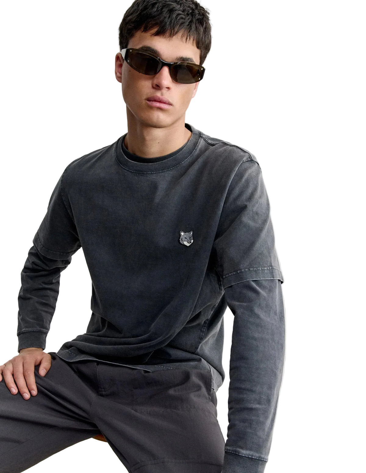 Hombre con gafas de sol y la camiseta Maison Kitsuné Fox Head Faded en gris oscuro sobre camiseta de manga larga, plano medio