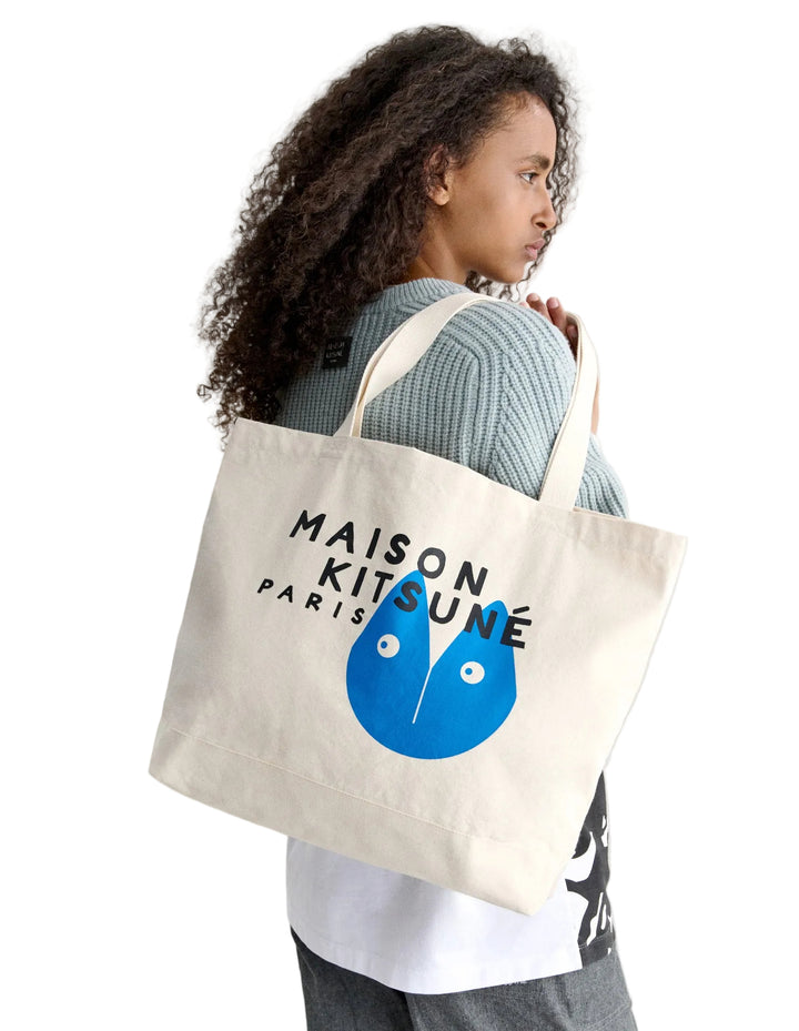 Modelo llevando al hombro el tote bag Maison Kitsuné ecru con estampado azul